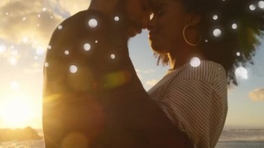 Gün batımı nda sahilde birbirine yakın Afrikalı-Amerikalı çift dijital kompozit ve beyaz bokeh ışıkları ön planda parlıyor.