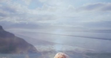 Eski beyaz bir kadının kollarını mutlu bir şekilde esneterek yakınlaşmak. Arkasında okyanus 4k bir arka plan