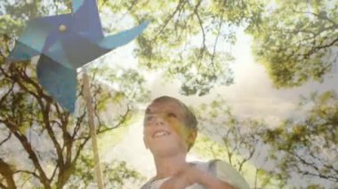 Parlak ve güneşli bir günde ormanda kağıt yel değirmeni ile oynayan beyaz bir çocuğun düşük açısı