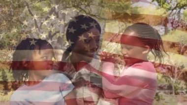 Arka planda bir Amerikan bayrağı sallayarak gösterirken parkta çocuklu askeri üniformalı bir Afrikalı-Amerikalı anne dijital kompozit