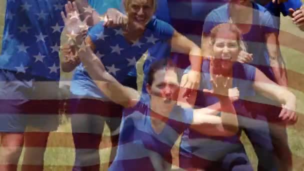 ポーズと背景をしながら青いシャツを着た多民族のグループのデジタルコンポジットは アメリカの旗を振って示しています — ストック動画