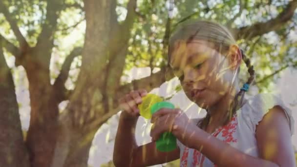 木と草の背景を持つ公園で泡を吹く白人の女の子のデジタルコンポジット — ストック動画