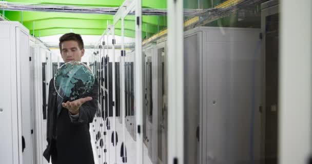 一位身穿西服的年轻白人男性技师的数码动画 举手表决 在一个服务器室的走廊上看到了一张地球全息图 — 图库视频影像