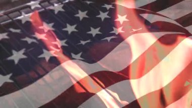 Ateşte Kızan sosislerin dijital bileşimi ve ön planda sallanan Bir Amerikan bayrağı