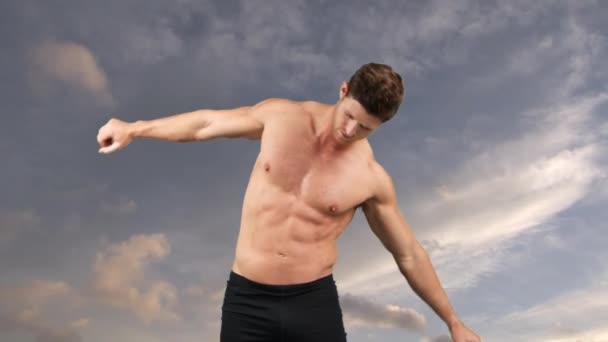 曇り空の背景に体を伸ばす白人のシャツのない男の正面図 — ストック動画