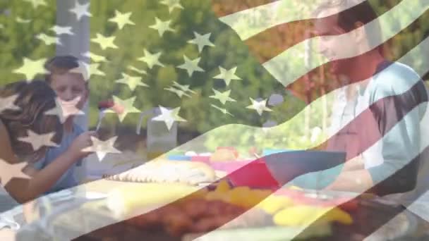 前景に手を振るアメリカの旗を持つピクニックバーベキューを持つ子供と家族のデジタルコンポジット — ストック動画