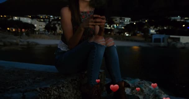 一位白种人妇女夜间坐在海滩边的数字合成材料和数字心脏在未来4K的飞行 — 图库视频影像