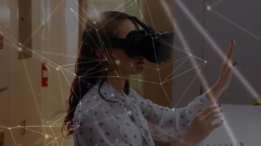 Ön planda sanal gerçeklik kulaklığı ve bağlantılı çizgiler ve noktalar takarken havada yazan beyaz bir kadının dijital kompoziti