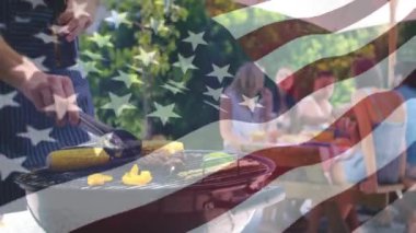 Ön planda sallayan bir Amerikan bayrağı ile bir piknik Barbekü arkadaşları için yemek pişirme bir adam dijital kompozit. Onun arkasında bir piknik masasında oturan arkadaşları hikayeler paylaşma görebilirsiniz