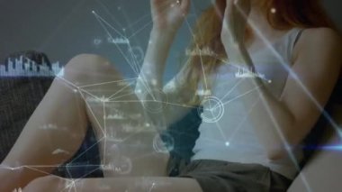 Ön planda bağlı çizgiler ve grafikler ile bir sanal gerçeklik kulaklık takarken bir kanepede oturan bir kadının yakın