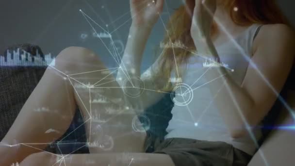 一个女人坐在沙发上 同时戴着虚拟现实耳机 在前景上连接线和图形的特写 — 图库视频影像