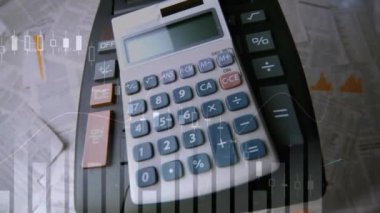 Ön planda çalışan grafikler ve istatistikler ile belgelerle dolu bir tabloya düşen iki hesap makinesinin dijital bileşimi