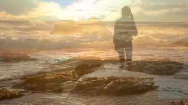 Gün batımında sahilde dururken kolları tamamen açık olan bir kadının dijital kompoziti