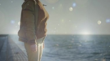 Kollar geniş açık ve bokeh ışık efektleri ile bir plaj duvarının kenarında duran bir kadının dijital kompozit