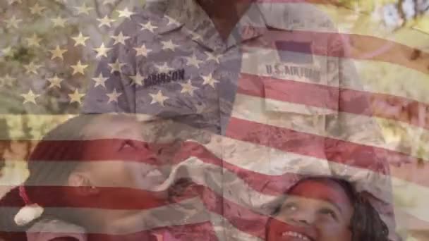 前景に手を振るアメリカの旗を持つ彼女の2人の娘を抱いた女性アフリカ系アメリカ人兵士のデジタルコンポジット — ストック動画