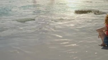 Ön planda akan kum ve suyun üzerinde oturan bir kadının dijital bileşimi.