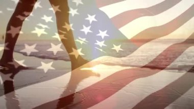 Gün batımında sahilde yürüyen bir kadının ve rüzgara karşı el sallayan Bir Amerikan bayrağının dijital kompoziti