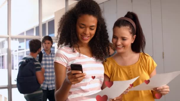 两个女孩在学校走廊阅读短信时表现出迷恋迹象的数字合成 数字心在前台慢慢飞舞 看到两个家伙在后台说话 — 图库视频影像