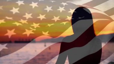 Gün batımında önünde Amerikan bayrağı dalgalanırken okyanusa bakan bir kadının dijital kompozitosu.
