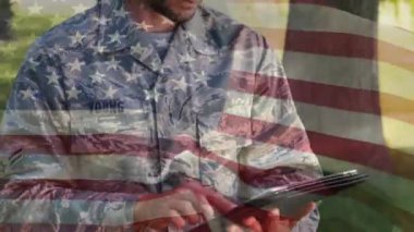 Ön planda sallanan Bir Amerikan bayrağı ile ağaçlarla çevrili parkta bir tablet üzerinde yazarak bir Amerikan askeri dijital kompozit