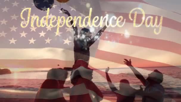 ビーチで祝う多様な友人のグループのシルエットと日没時に風船を持つ女性のデジタルコンポジット アメリカの旗は7月4日の金独立記念日のテキストの後ろに波 — ストック動画