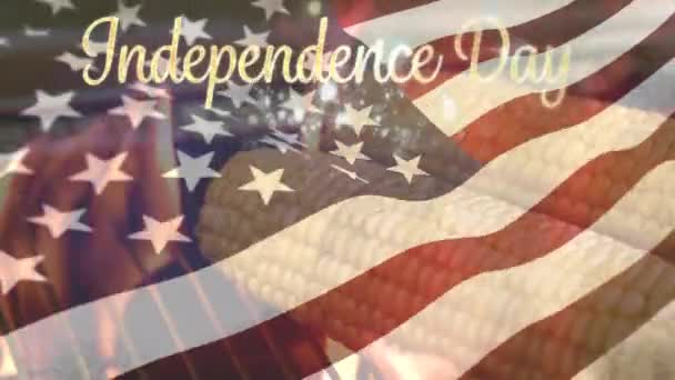 7月4日 玉米被烤的玉米数字复合物 美国国旗在金色独立日文字后面挥舞着 带有散景灯 — 图库视频影像