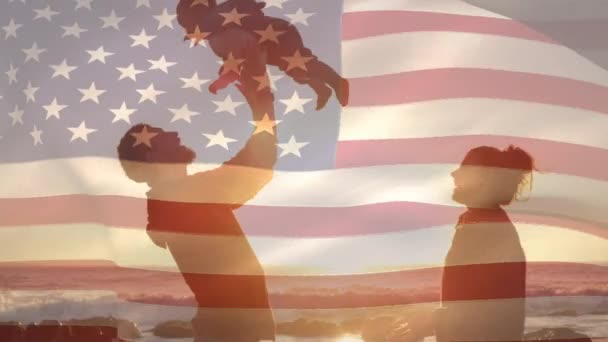 在海滩 父亲在日落时举起婴儿的剪影 而美国国旗在7月4日的背景中挥舞 — 图库视频影像