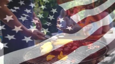 Farklı bir grup arkadaş piknik masasında ve arka planda Bir Amerikan bayrağı dalgaları oturup bir adam barbekü dijital kompozit.