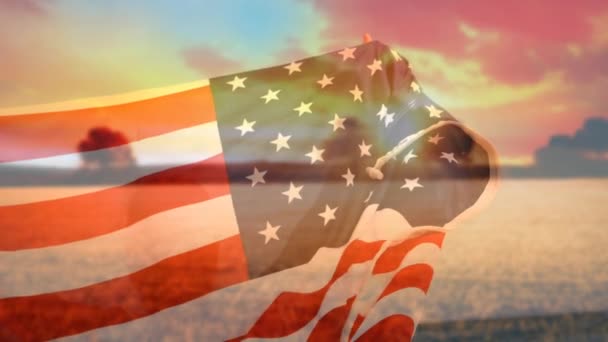 背景が海の上に沈む太陽を示している間 アメリカの旗を持つ男のデジタルコンポジット — ストック動画