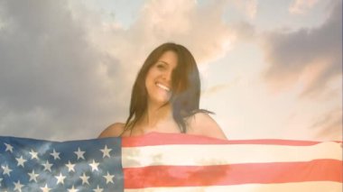 Gülümserken Amerikan bayrağı tutan Beyaz kadının dijital bileşimi. Arka plan bulutlarla gökyüzünü gösterir.