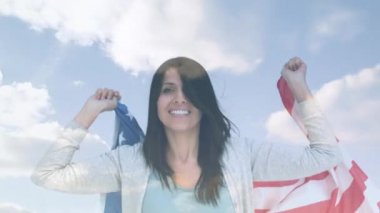 Arka plan bulutlar ile gökyüzü gösterirken Amerikan bayrağı gülümseyen ve dans tutan Kafkas kadın dijital kompozit