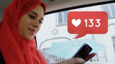 Hareketli bir aracın içinde cep telefonu kullanarak başörtüsü takan güzel karışık ırk lı kadının dijital kompoziti. Kırmızı mesaj kabarcık simgesi içinde artan numaraları ile Kalp simgesi sosyal medya için ekranın sağ tarafında gösterir.