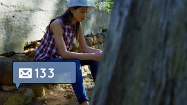 Cep telefonu kullanırken oturan Beyaz kadının dijital bileşimi. İleti balonu simgesinin içindeki zarf simgesi ve artan sayılar ekranın sol alt köşesinde görünür.