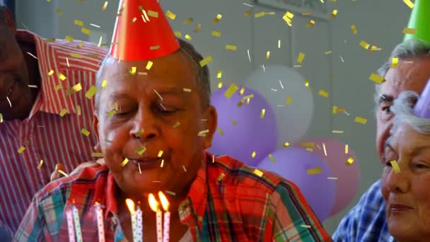 屋内で誕生日を祝う多民族の先輩のアニメーション 誕生日ケーキにろうそくを吹き パーティーの帽子をかぶる一方 黄金のコンフェッティは前景に落ちています — ストック動画