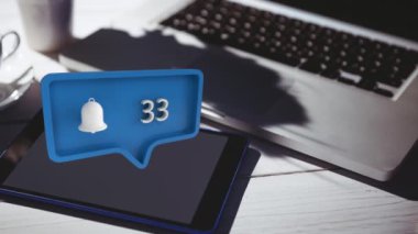 Bir dizüstü bilgisayar ve tablet ile bir masanın dijital kompozit bildirim simgesi ve artan numaraları ile mavi bir mesaj balonu sosyal medya için ekranda hareket ederken