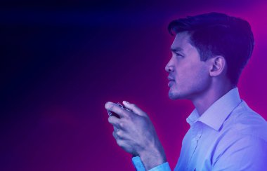 Turkuaz ve mor arka plana karşı video oyunu oynayan genç işadamının yan görünümü