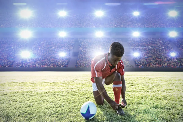 ラグビー選手は 混雑したサッカースタジアムのデジタル画像に対してフィールド上の靴ひもを結ぶ — ストック写真