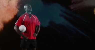 Renkli toz siyah bir arka plan 4k karşı düşerken genç bir Afro-Amerikan erkek rugby oyuncusu etrafa bakarak ve kolunun altında bir top tutarak Animasyon