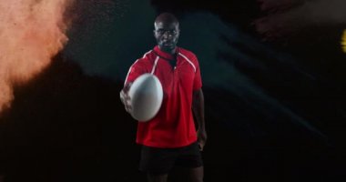 Renkli toz siyah bir arka plan 4k karşı düşerken, kamera arayan genç bir Afro-Amerikan erkek rugby oyuncusu animasyon, oyun ve bir top ile işaret