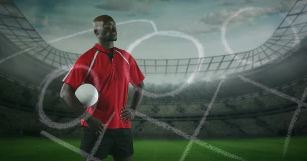 アフリカ系アメリカ人の男子ラグビー選手が立ち ボールを腕の下に抱き 手描きのゲームプランを背景に4Kの前景とスポーツスタジアムで見回すアニメーション — ストック動画