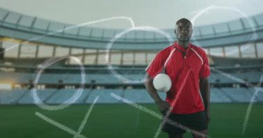 Animasyon bir Afro-Amerikan erkek rugby oyuncusu ayakta, kolunun altında bir top tutarak ve arka planda 4k ön planda ve spor stadyumunda elle çizilmiş oyun planı ile kameraya bakıyor