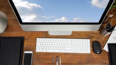 Bir masa üzerinde klavye, tablet, akıllı telefon, fare ve kalem konteynerile bilgisayar monitöründe görüntülenen mavi gökyüzü ve bulutların animasyonu, havai görünüm
