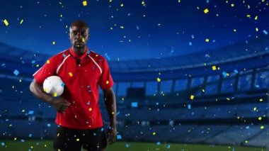 Bir top tutan ve arka planda mavi ve sarı konfeti düşen ve spor stadyum ile kameraya bakan bir Afro-Amerikan erkek rugby oyuncusu Animasyon