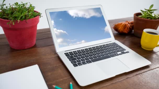 蓝天上的云动画显示在笔记本电脑屏幕上 桌上有咖啡杯和植物盆 — 图库视频影像
