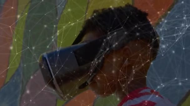 前景に浮かぶ接続のネットワークのアニメーション 背景にVrヘッドセットを装着したアフリカ系アメリカ人の少年のクローズアップ — ストック動画
