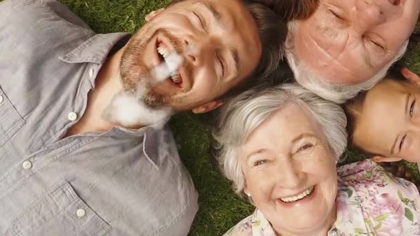 三世代の白人の家族が笑顔で草の上に円の中に寝そべって浮かぶ雲の家の形のアニメーション — ストック動画