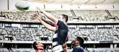 Takım üyeleri güneşli bir günde stadyumda topu havada tutmaya çalışırken farklı erkek rugby oyuncularının yan görüntüsü.