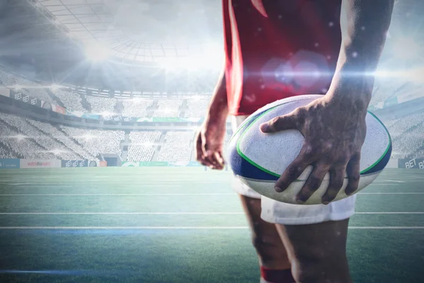 Rugby player holding rugby ball against stadium against sky