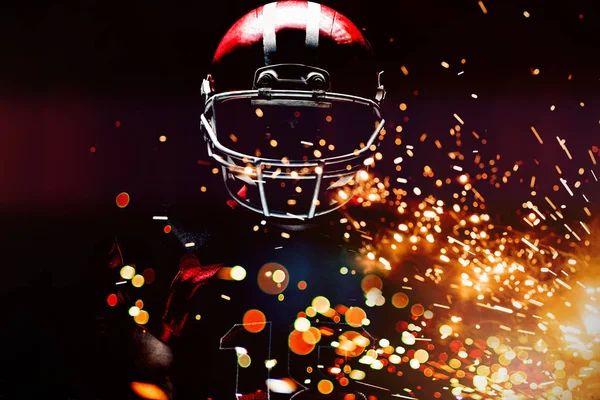 American football player standing in helmet against firework bursting sparkle background