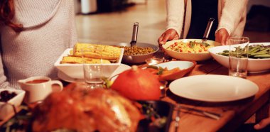 İki kadının ön tarafı, biri masada oturuyor, diğeri ayakta ve Şükran Günü yemeğinde arkadaşlarına servis yapmak için bir tabak yemek tutuyor.